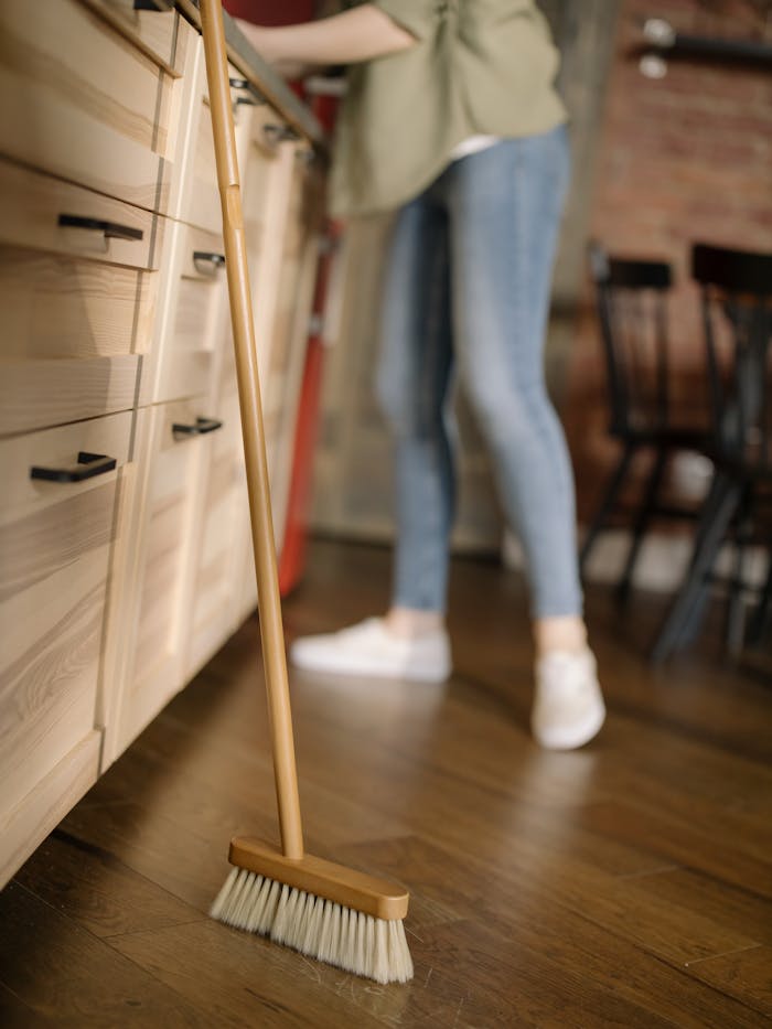 digital A woman in casual attire sweeps the kitchen floor, maintaining cleanliness in a cozy home.
